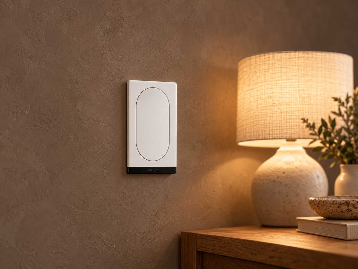 White StellarTrack wall switch beside a warmly lit living room with a table lamp.