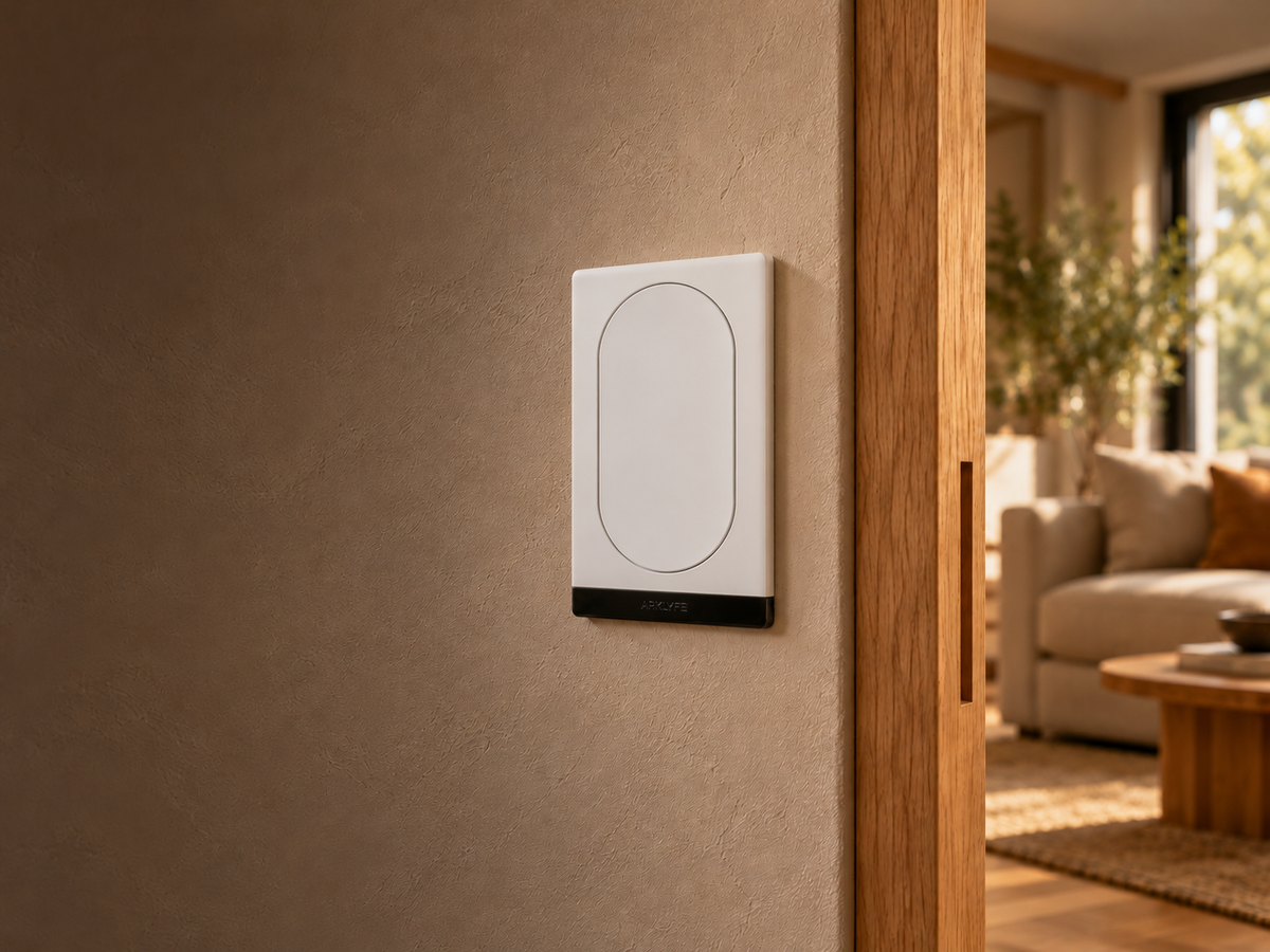 White one-button StellarTrack switch on a warm plaster wall beside a softly lit home interior.