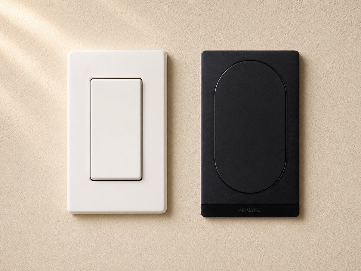 Side-by-side comparison of a white traditional Clipsal-style smart switch and a matte black Arklyfe Matter smart switch on a warm cream Australian plaster wall